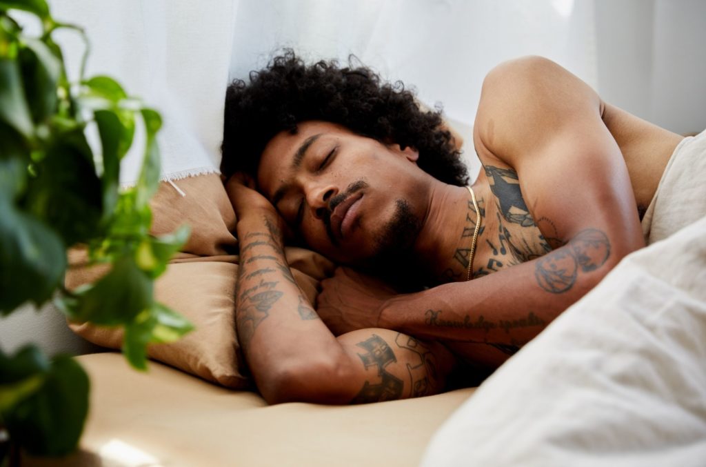 young man with tattoos sleeping after treating insomnia symptoms and causes