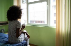 young woman with alcohol anxiety looking out window with tea cup
