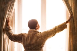 woman waking up with hangover depression after drinking opening curtains