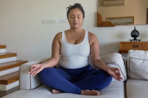 young woman meditating on couch taking care of mental health symptoms with mindfulness practice