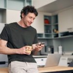 Man reading a smartphone while holding a cup of coffee, considering the risks of drinking alcohol while taking Zoloft® and its potential effects on health.