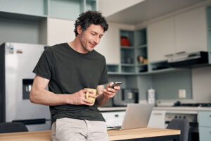 Middle-aged man holding a cup of coffee and browsing his smartphone in search for information about Viagra® myths online.