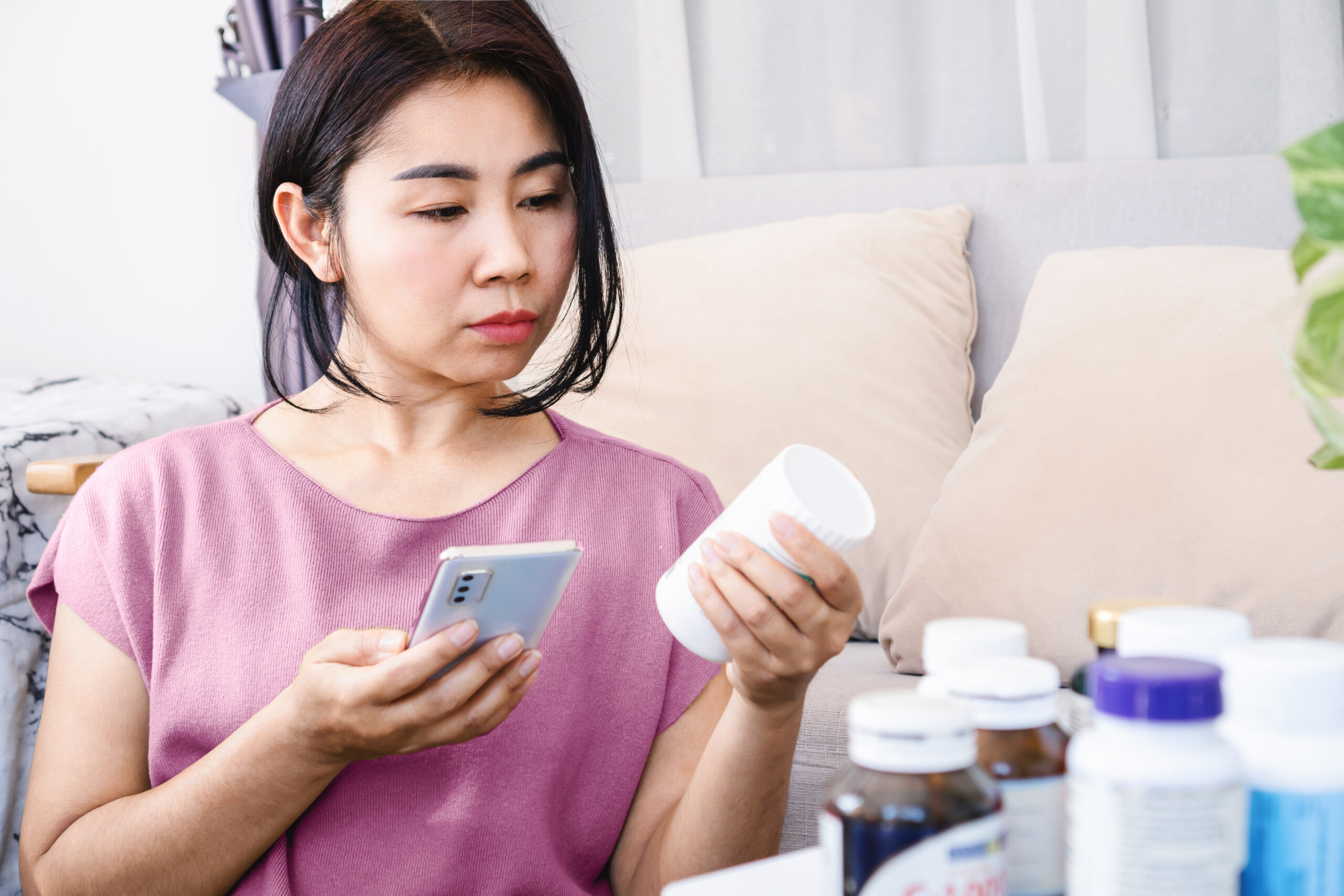 A woman intently reading information on her smartphone while holding a bottle of medication, researching effective treatments for genital herpes.