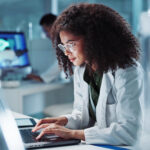 A woman working on a laptop in a modern lab, researching the latest advancements in herpes treatment.