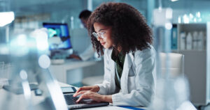 A woman working on a laptop in a modern lab, researching the latest advancements in herpes treatment.