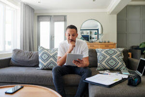 Young man sitting on a couch, deep in thought, considering whether Cialis® or Viagra® is the right choice for him.