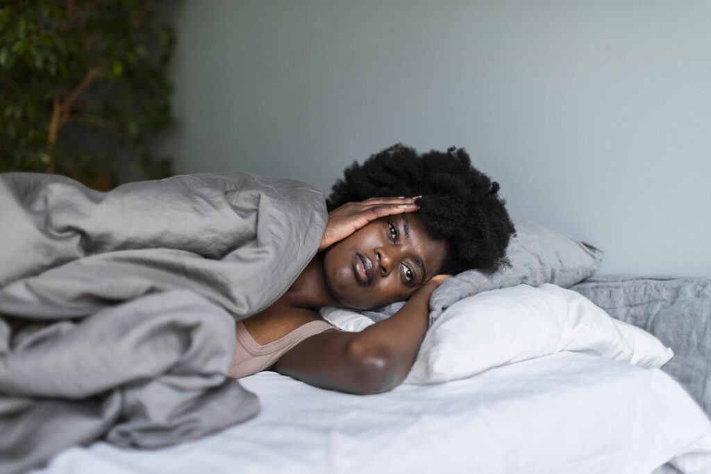 A young woman lying in bed in pain, holding her head, illustrating the struggles and misconceptions associated with insomnia.