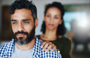 A man gazing with a contemplative expression while a woman offers support with her hand on his shoulder, representing empathy and the importance of support in understanding and managing depression