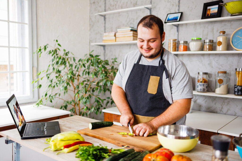 8 Ways You Can Reduce or Stop Hair Loss, featuring tips like gentle hair care and a healthy diet, displayed next to a man chopping fresh vegetables in a bright kitchen, following a recipe from his laptop.