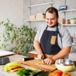 8 Ways You Can Reduce or Stop Hair Loss, featuring tips like gentle hair care and a healthy diet, displayed next to a man chopping fresh vegetables in a bright kitchen, following a recipe from his laptop.