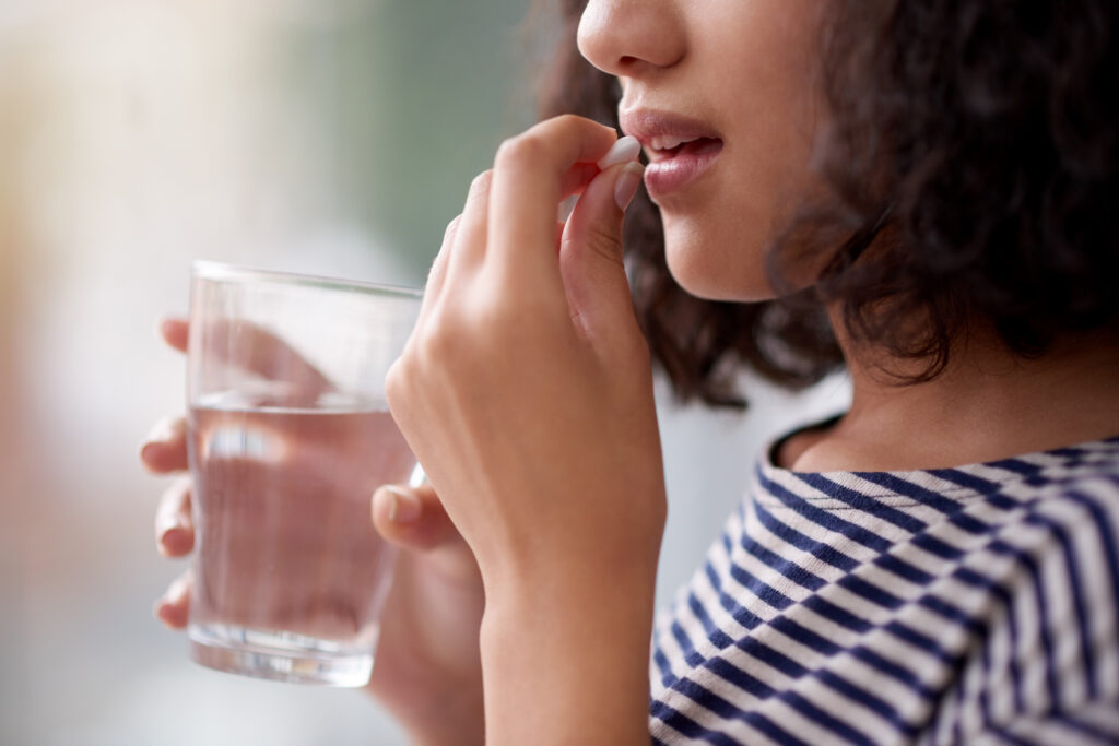 A close-up of a woman holding a glass of water and taking a pill, representing the use of Errin birth control. The image highlights medication use and personal health care choices.