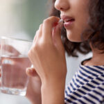 A close-up of a woman holding a glass of water and taking a pill, representing the use of Errin birth control. The image highlights medication use and personal health care choices.