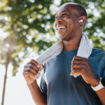 Smiling middle-aged bald man outdoors with a towel around his neck, reflecting positive results from hair loss treatment.