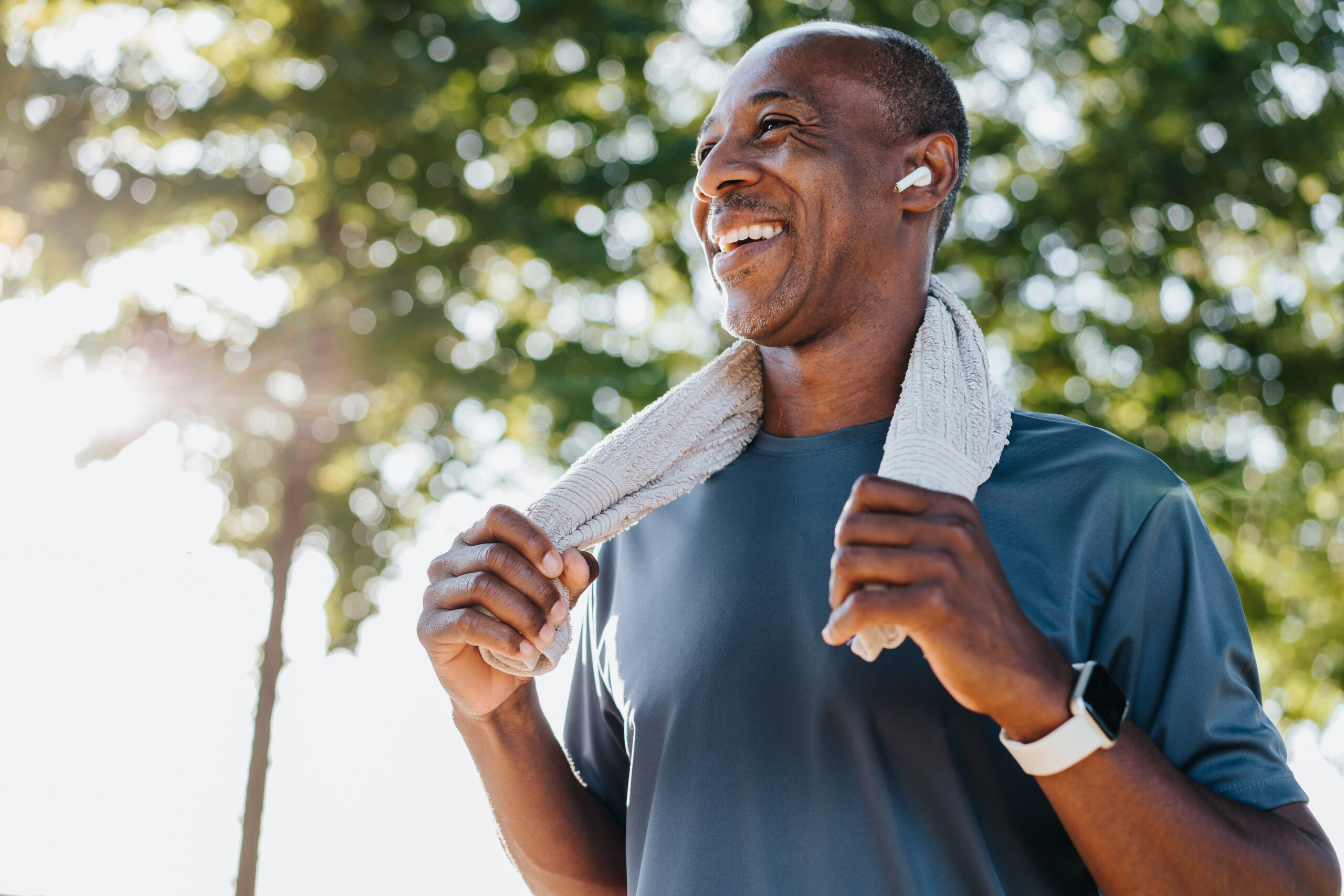 Smiling middle-aged bald man outdoors with a towel around his neck, reflecting positive results from hair loss treatment.