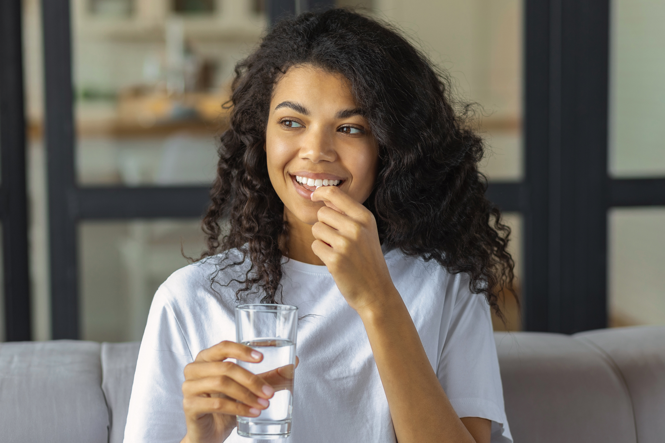 A woman smiling and holding an escitalopram (Lexapro®) pill and a glass of water, taking her medication to manage depression and anxiety.