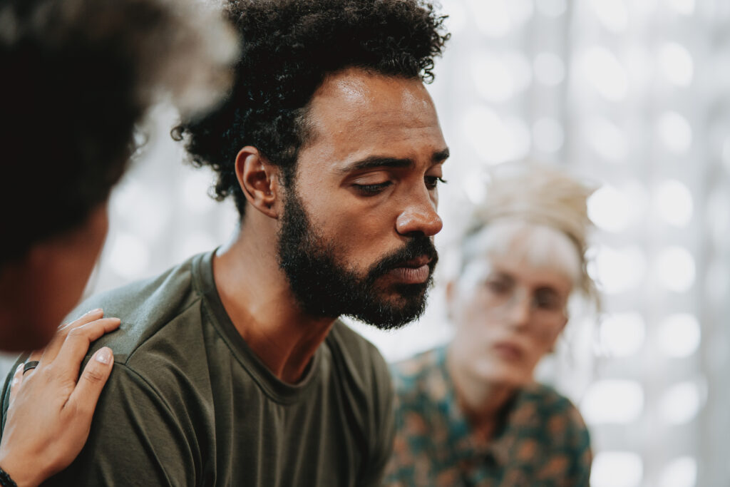 Man being comforted in a support group, highlighting the importance of support and treatment options like fluoxetine (Prozac®) for managing mental health conditions.