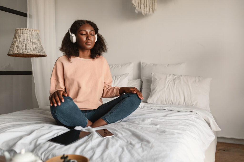 A woman meditating with closed eyes and headphones on, practicing mindfulness in a peaceful bedroom, symbolizing coping strategies for managing anxiety and promoting mental well-being