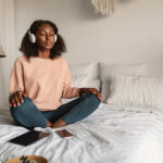 A woman meditating with closed eyes and headphones on, practicing mindfulness in a peaceful bedroom, symbolizing coping strategies for managing anxiety and promoting mental well-being