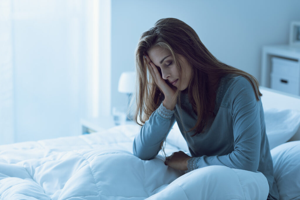 Woman awake at night, touching her forehead in distress, illustrating the challenges of insomnia and the need for effective treatment and coping strategies