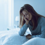 Woman awake at night, touching her forehead in distress, illustrating the challenges of insomnia and the need for effective treatment and coping strategies