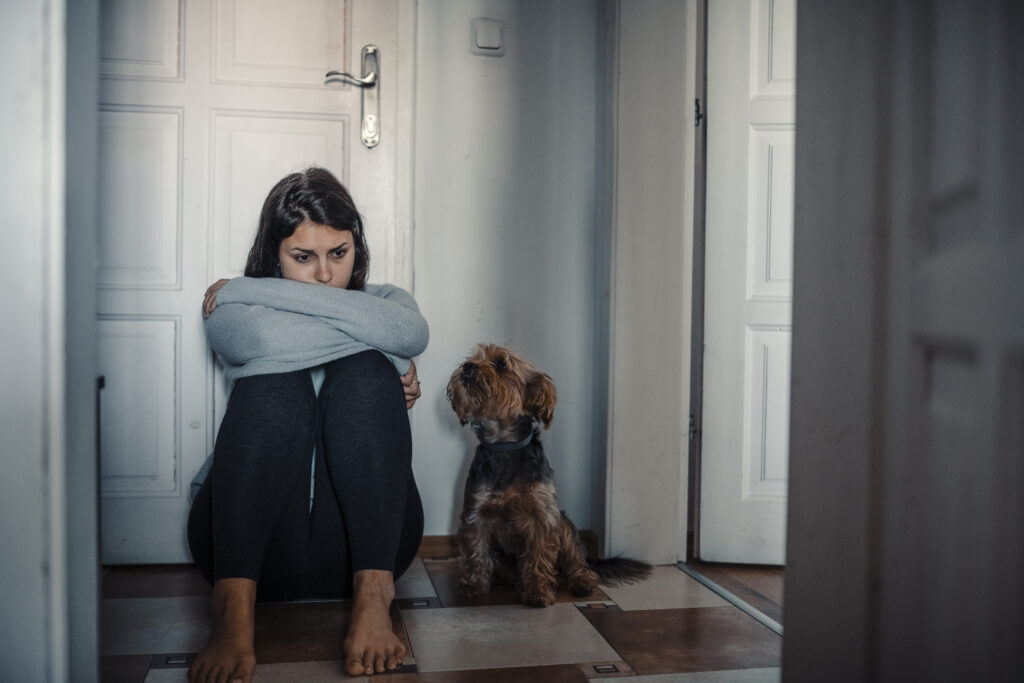 Woman sitting exhausted on the floor with her dog, illustrating the emotional challenges of living with obsessive-compulsive disorder (OCD) and the importance of seeking support and treatment.