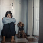 Woman sitting exhausted on the floor with her dog, illustrating the emotional challenges of living with obsessive-compulsive disorder (OCD) and the importance of seeking support and treatment.