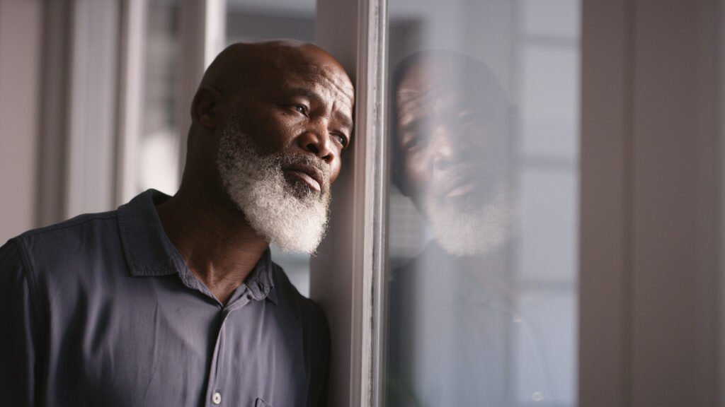 A man leaning on the window, looking pensive and overwhelmed, reflecting the emotional struggles of depression and the importance of understanding medication options for treatment.