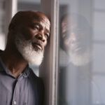 A man leaning on the window, looking pensive and overwhelmed, reflecting the emotional struggles of depression and the importance of understanding medication options for treatment.