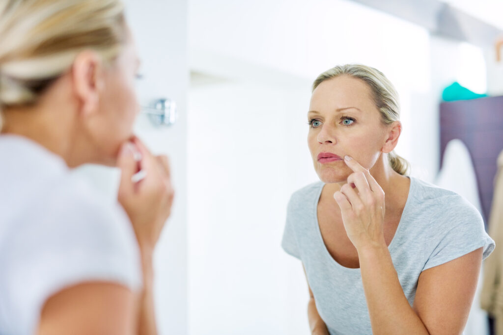 Woman examining her skin, managing cold sores, and taking care of her skin health.