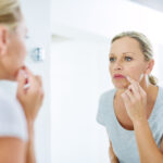 Woman examining her skin, managing cold sores, and taking care of her skin health.