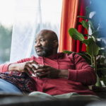 A bald man looking out the window, contemplating health and wellness, representing the importance of understanding finasteride's side effects in men.