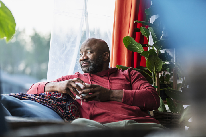 A bald man looking out the window, contemplating health and wellness, representing the importance of understanding finasteride's side effects in men.