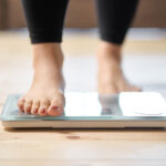 A woman stepping onto a weigh scale, symbolizing the process of tracking progress toward SMART weight loss goals for the New Year.