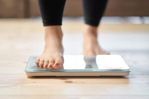 A woman stepping onto a weigh scale, symbolizing the process of tracking progress toward SMART weight loss goals for the New Year.