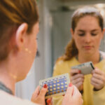 A woman holding birth control pills, checking the expiration date to determine if the medication is still safe to take after it has expired.