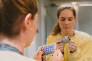 A woman holding birth control pills, checking the expiration date to determine if the medication is still safe to take after it has expired.