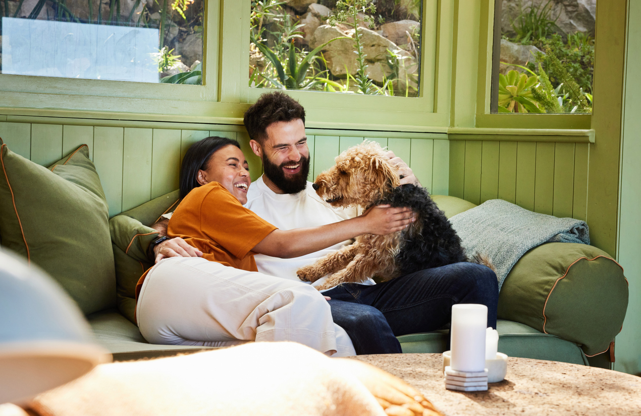 A laughing couple playing with their dog on the living room sofa, symbolizing the positive impact of ED medication on overall well-being and healthy relationships.