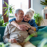 A happy couple sitting together on a sofa at home, researching on a laptop to learn more about whether Viagra® is the right treatment option for them.