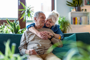 A happy couple sitting together on a sofa at home, researching on a laptop to learn more about whether Viagra® is the right treatment option for them.