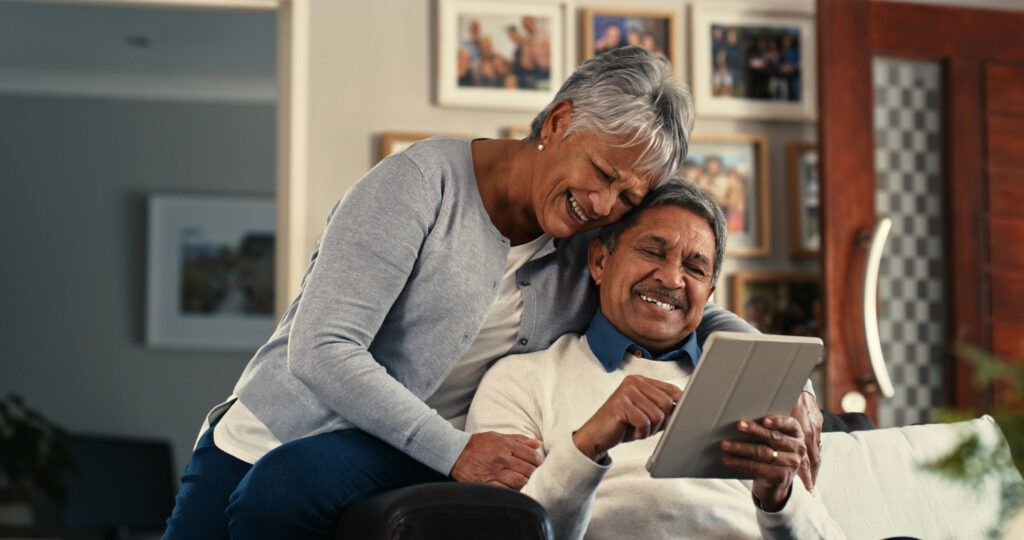 Couple sitting together on a sofa, researching the safe use of Viagra® and Cialis® for erectile dysfunction on a digital tablet.