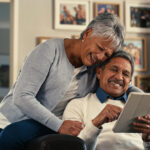 Couple sitting together on a sofa, researching the safe use of Viagra® and Cialis® for erectile dysfunction on a digital tablet.