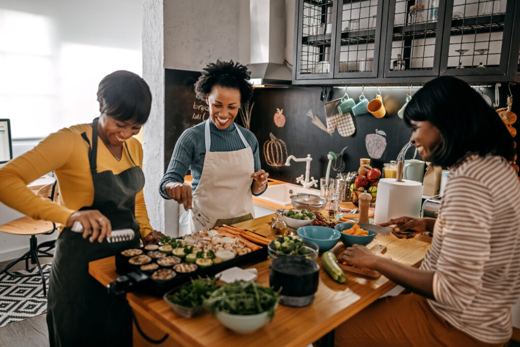 Three female friends cooking a healthy meal together in the kitchen, emphasizing the importance of balanced meals and mindful eating for sustainable weight loss after the holidays.