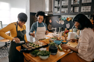 Three female friends cooking a healthy meal together in the kitchen, emphasizing the importance of balanced meals and mindful eating for sustainable weight loss after the holidays.