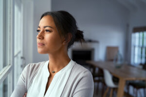 Woman gazing out of a window, reflecting on the persistent challenges of dysthymia, a form of depression that requires careful understanding and treatment.