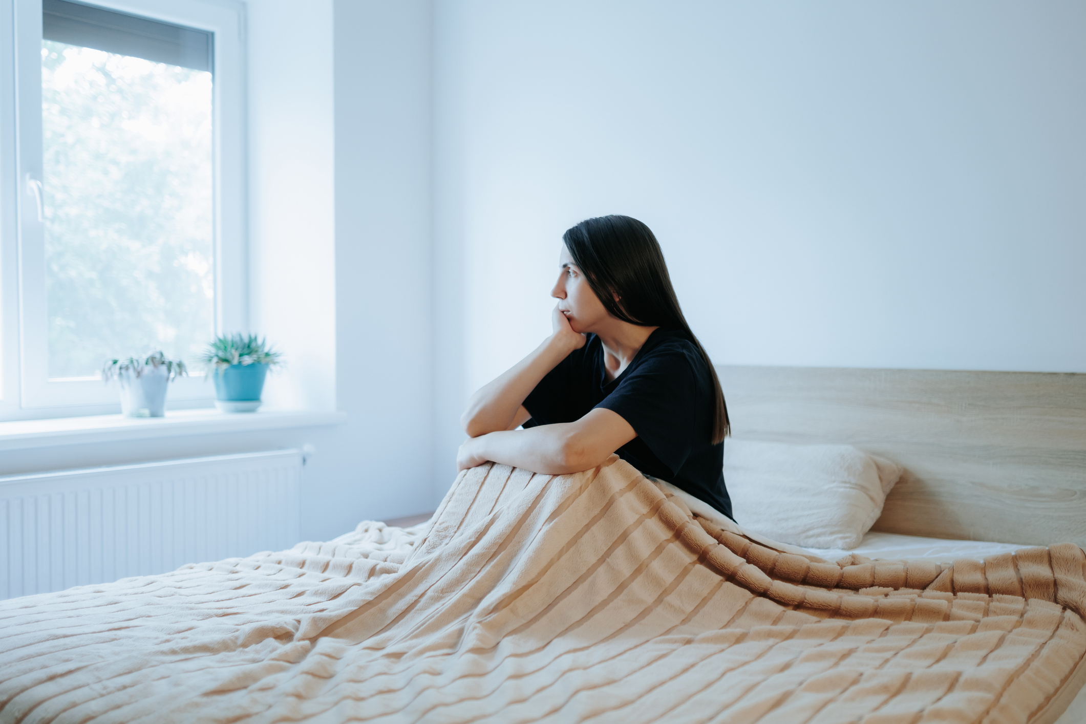 Woman sitting alone in a bedroom at night, looking unhappy, reflecting the emotional struggles associated with seasonal affective disorder (SAD)