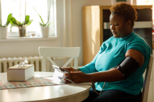 A woman checking her blood pressure at home, symbolizing the importance of monitoring and managing high blood pressure to prevent serious health risks.