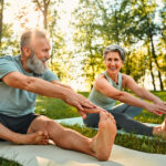 Man and woman stretching on a yoga mat outdoors, highlighting the role of a healthy lifestyle in supporting Cialis® effectiveness.