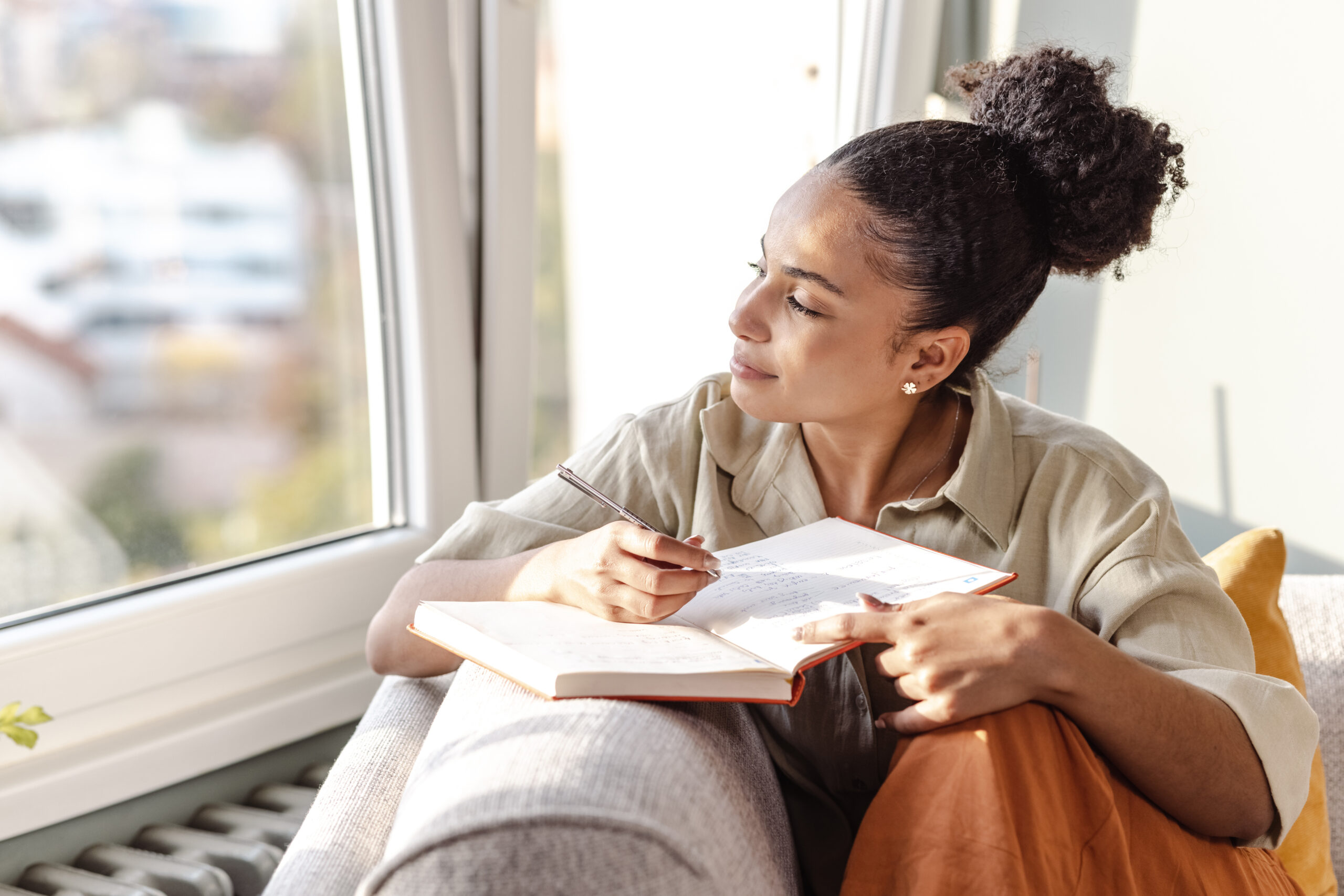 A woman writing notes in a notebook, symbolizing the reflective process of therapy to identify emotional triggers and support weight loss goals.