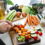 A woman cutting fresh vegetables on a kitchen counter, emphasizing the role of nutrition in medical weight loss programs and healthy meal preparation.