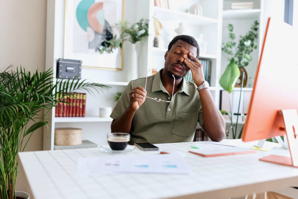 Man sitting at his desk with glasses off, rubbing his eyes, showing the side effects of his new medication, amitriptyline.